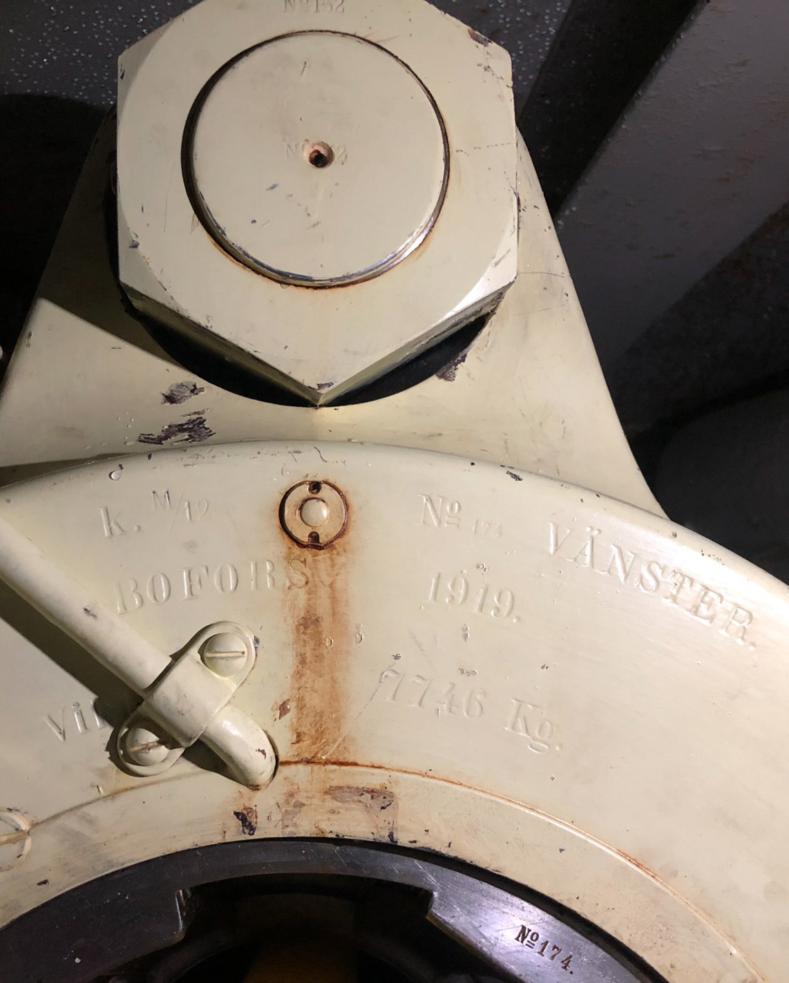 Närbild på laddningsmynning av en kanon. Metall, sladdar och skruvar målat i beige. Stämplat i metallen kring öppningen "15 cm K m/12 nr 174 Vänster Bofors 1919 vikt 7746 kg".
