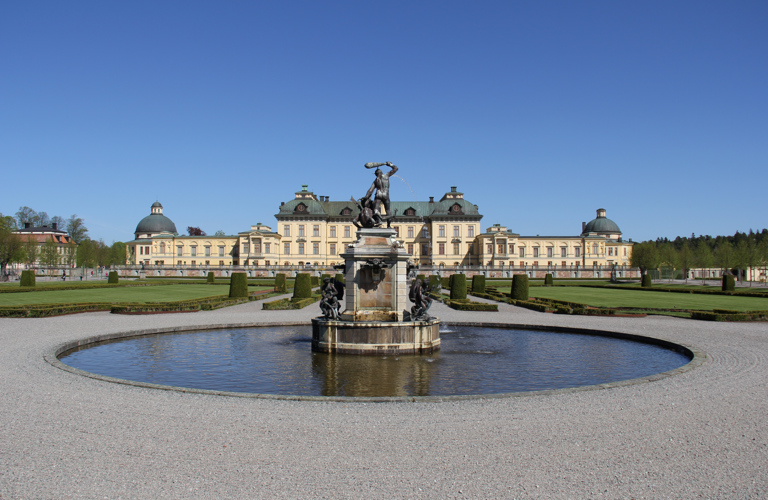Drottningholms slott sett från barock-trädgården. I förgrunden en fontän med en skulptur.