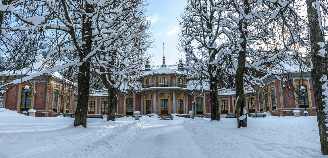 Kina slott, Drottningholm. Ett litet rosa slott med gulmålade snickerier kring dörrar och fönster. Vinter och snö.