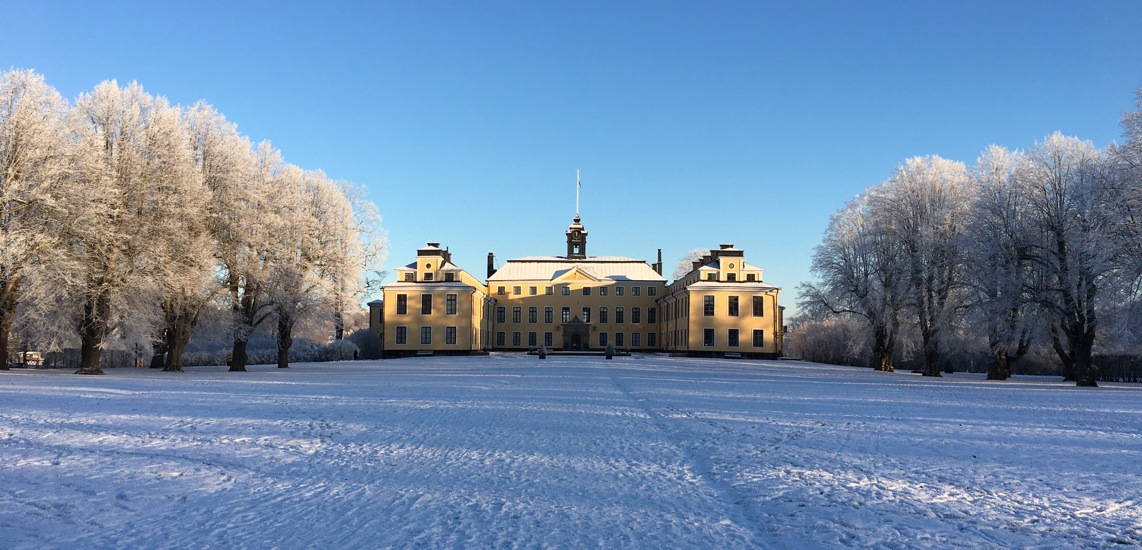Ulriksdals slott. Ljusgult slott med flygelbyggnader sett över en stor gräsyta. Vinter och snö.
