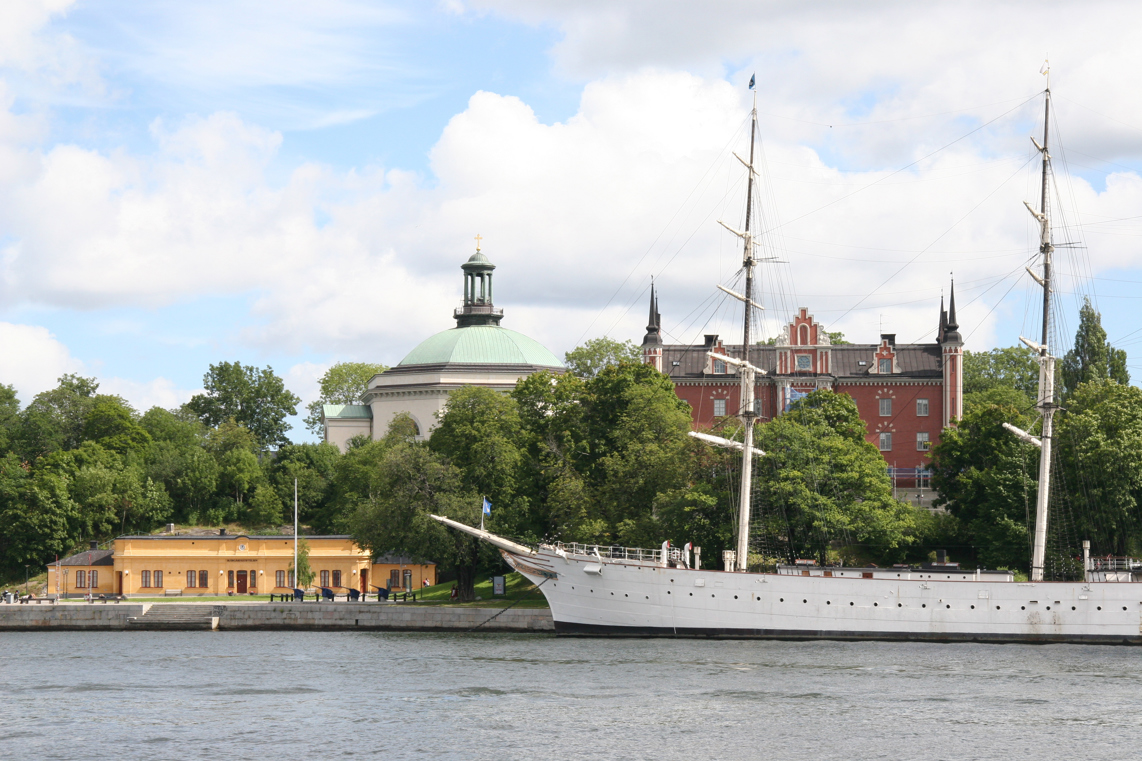 Skeppsholmen med Högvakten, Skeppsholmskyrkan, Amiralitetshuset och skeppet Af Chapman. Sommar och grönska.