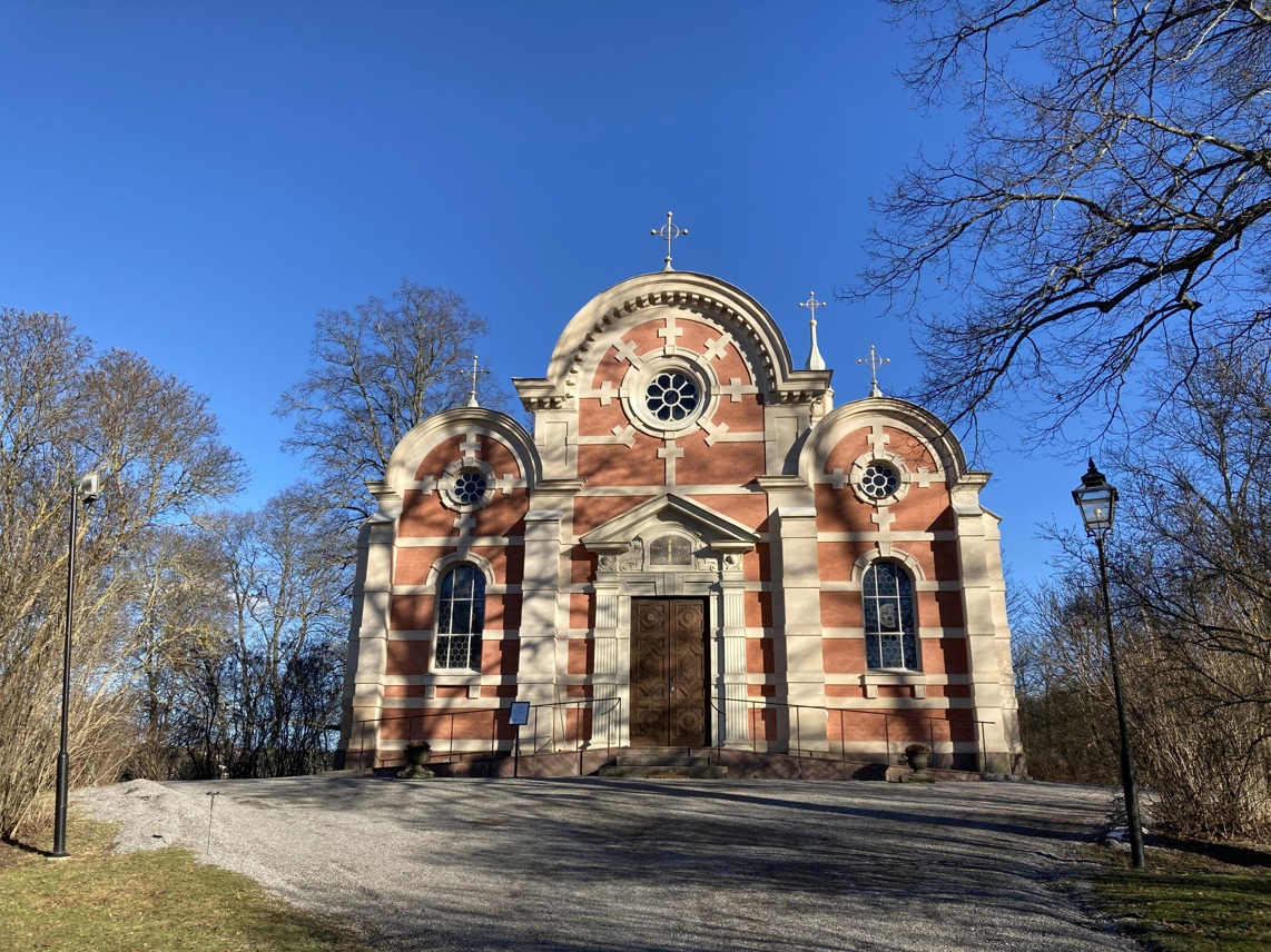 Slottskapellet vid Ulriksdal. Rosa byggnad med rundade former och ljusgrå stendekor. Tidig vår.