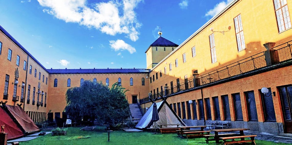 Innergården till historiska museet i Stockholm. På gräsytan står några bänkbord och ett par vikinga-inspirerade tält.