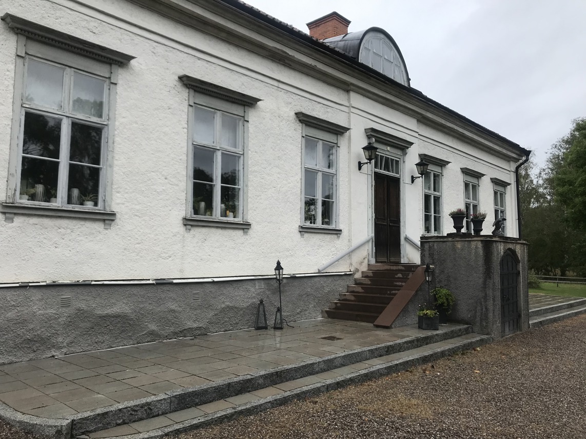 Mangårdsbyggnaden på Herrsäter. En vitputsad envåningsbyggnad med halvmåneformad tak-kupa,