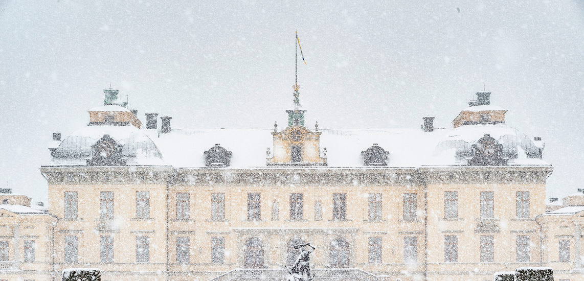 Slottet sett från parken på baksidan med en staty i mitten och snön som faller ner framför slottet.