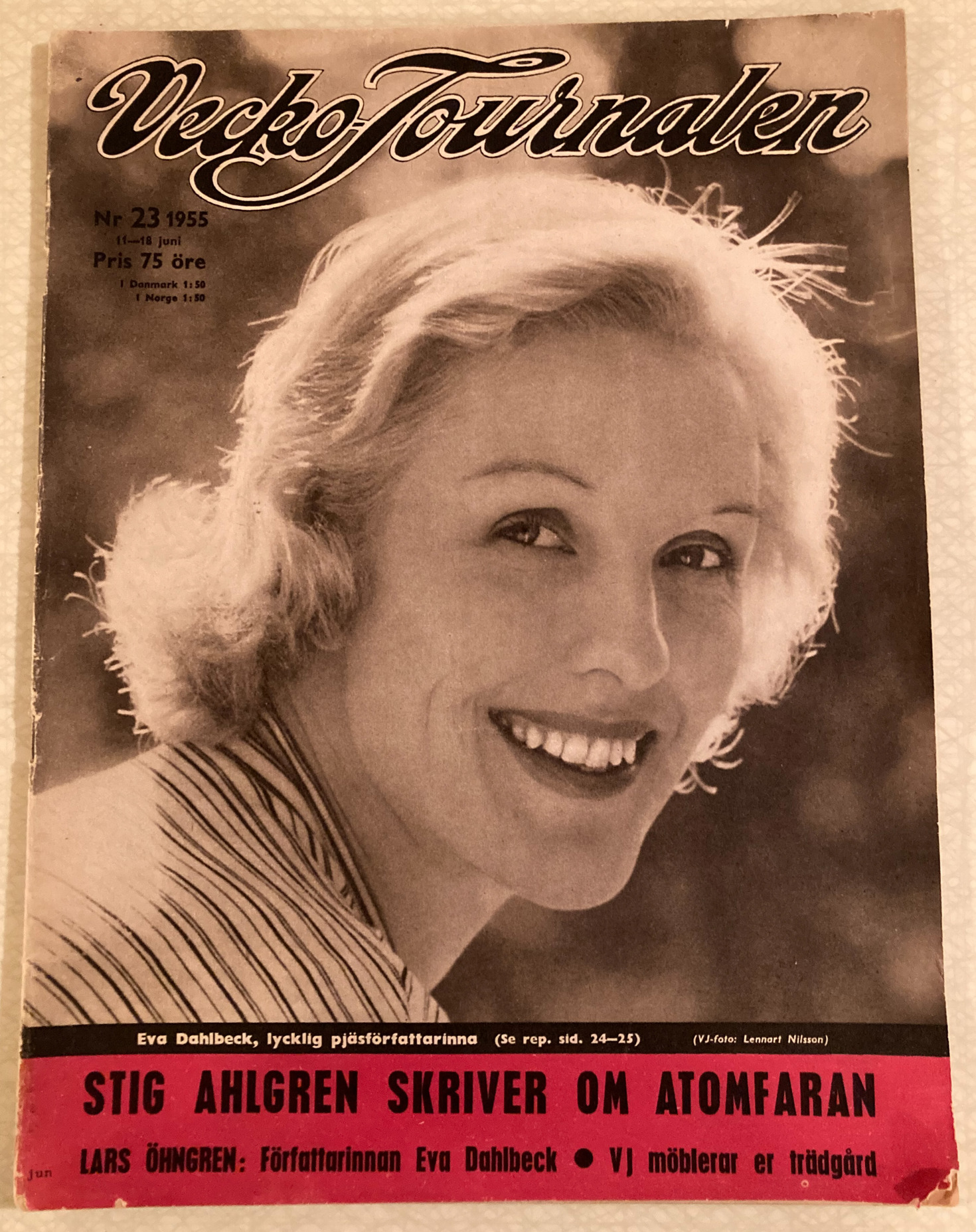 En gammal "Veckojournalen" från 1955. Ett svarttvitt fotografi visar en leende kvinna. Längst ned på tidningen står att läsa "Stig Ahlgren skriver om atomfaran"